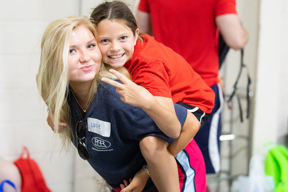 A young girl shows the peace sign as she rides piggyback on the back of a pharmacy student | Pharmacy School | Presbyterian College | Clinton SC